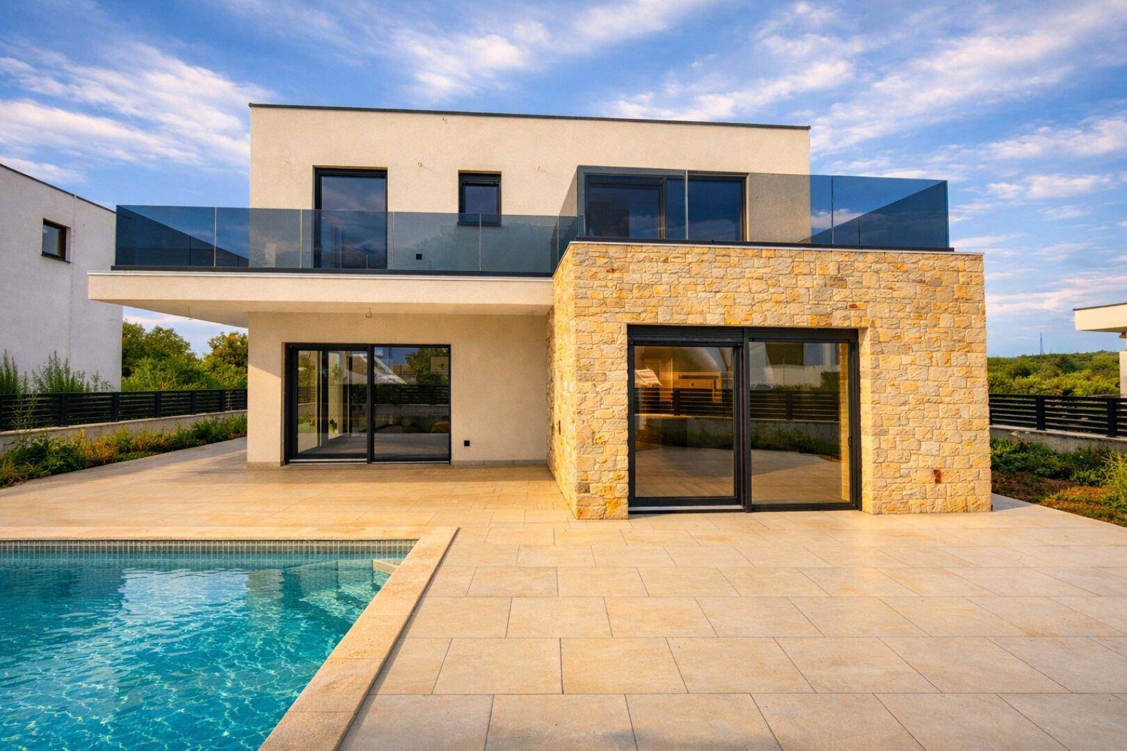 Moderne Villa mit Pool und großer Terrasse, umgeben von Natur unter blauem Himmel.