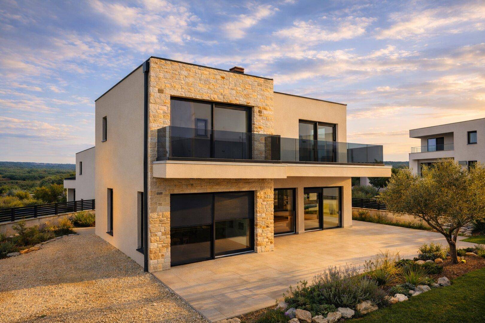 Moderne Villa mit Steinfassade und großer Terrasse in ländlicher Umgebung bei Sonnenuntergang.