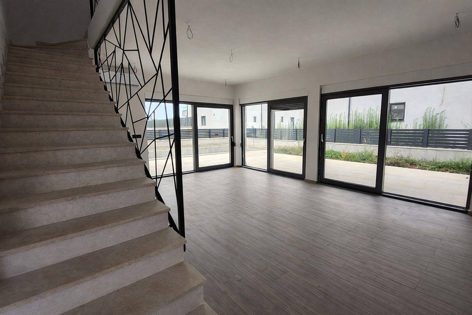 Geräumiger Wohnbereich mit großen Fensterfronten und Treppe in einem Neubau.