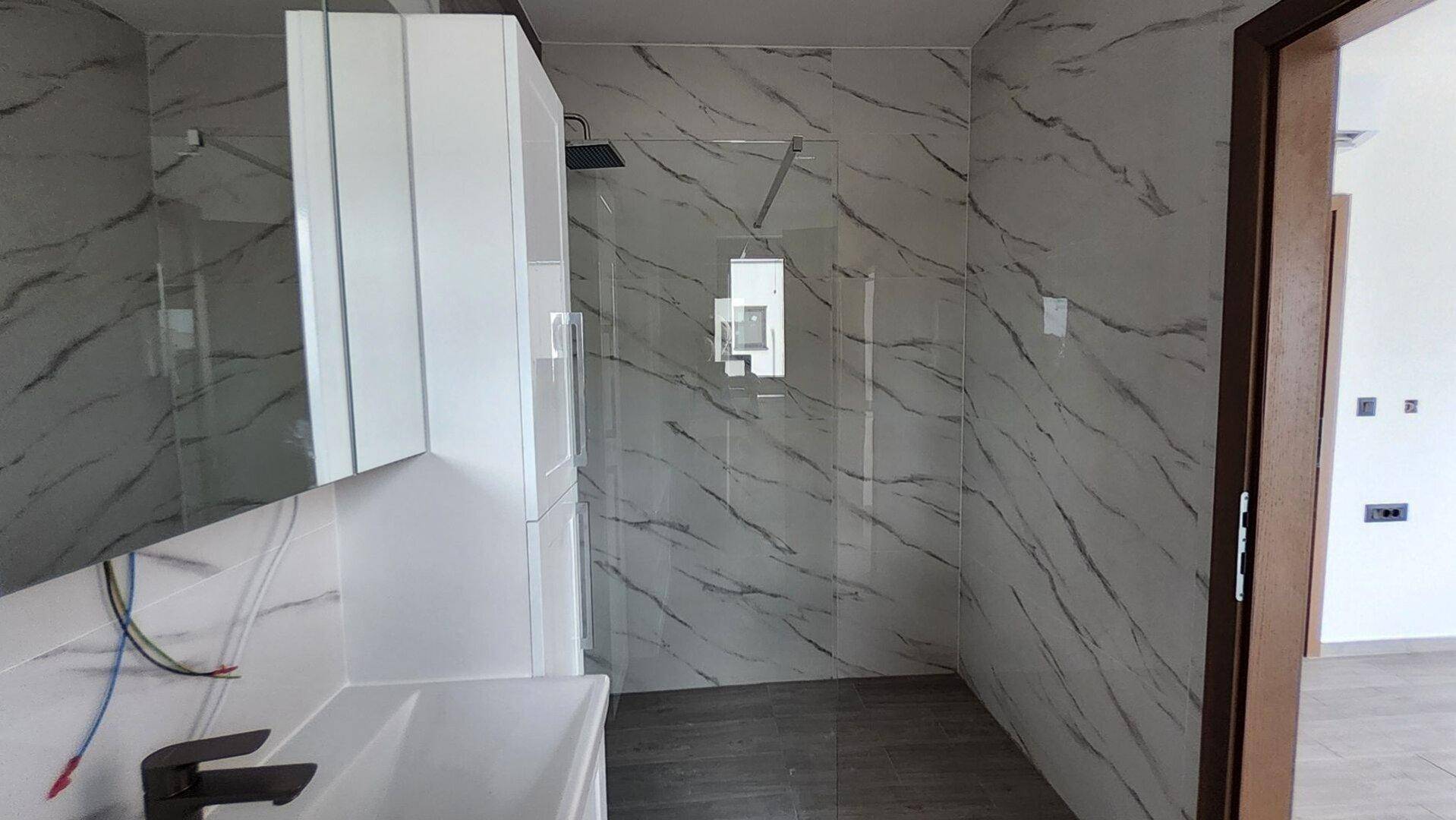 Modernes Badezimmer mit großformatigen Fliesen, Dusche und weißem Waschtischunterschrank.