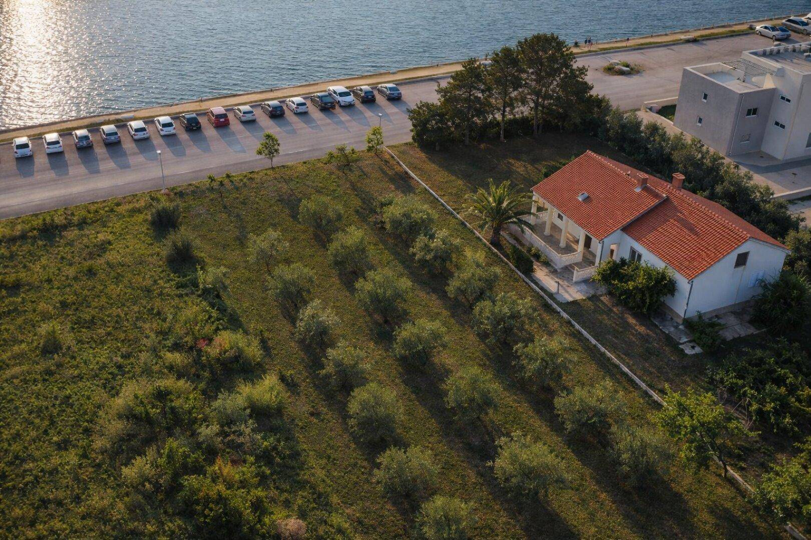 Luftaufnahme eines traditionellen Hauses mit Ziegeldach und Olivenhain nahe dem Meer.