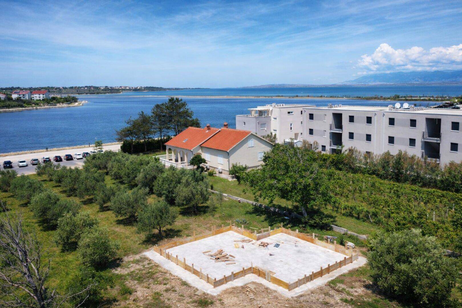 Luftaufnahme eines Baugrundstücks mit Fundament neben einem bestehenden Haus und Meerblick.