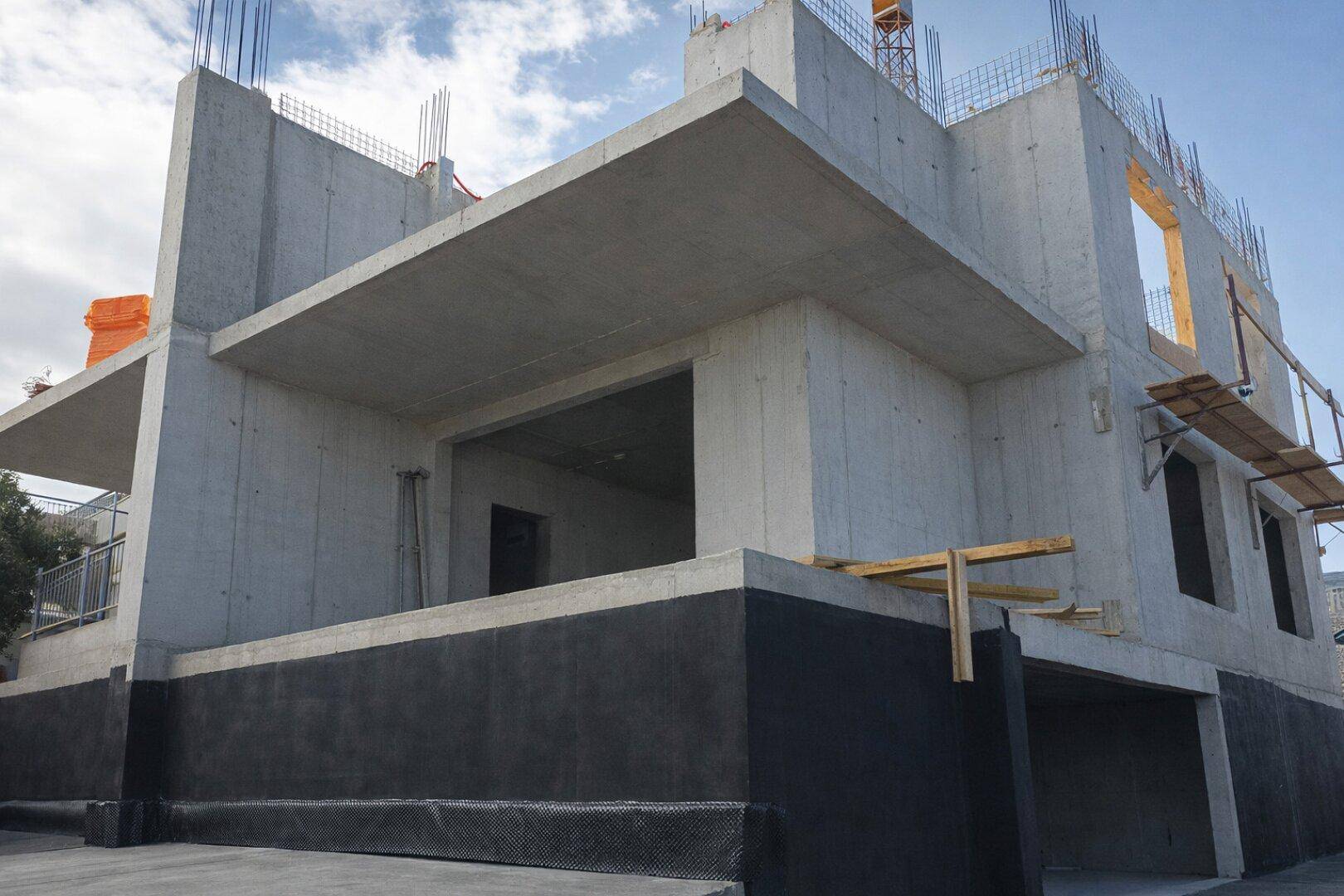 Rohbau eines modernen Gebäudes aus Beton mit sichtbaren Bewehrungsstäben und Flachdach.