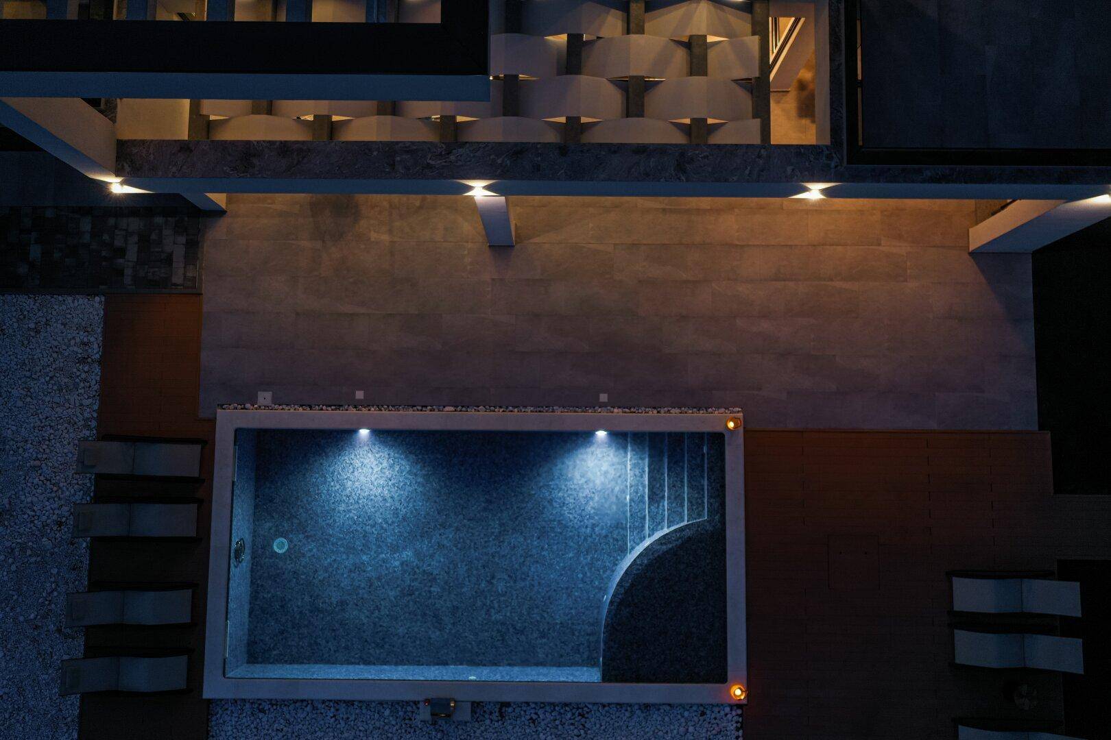 Draufsicht auf den beleuchteten Poolbereich der modernen Villa bei Nacht.