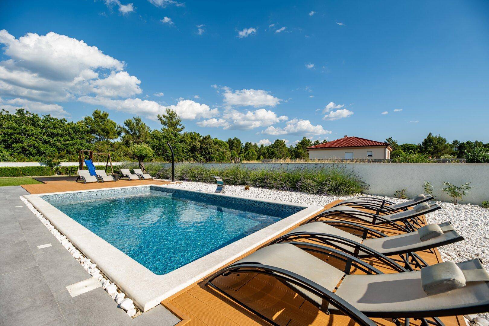 Sonniger Poolbereich mit Liegestühlen, umgeben von einem gepflegten Garten und mediterraner Bepflanzung.