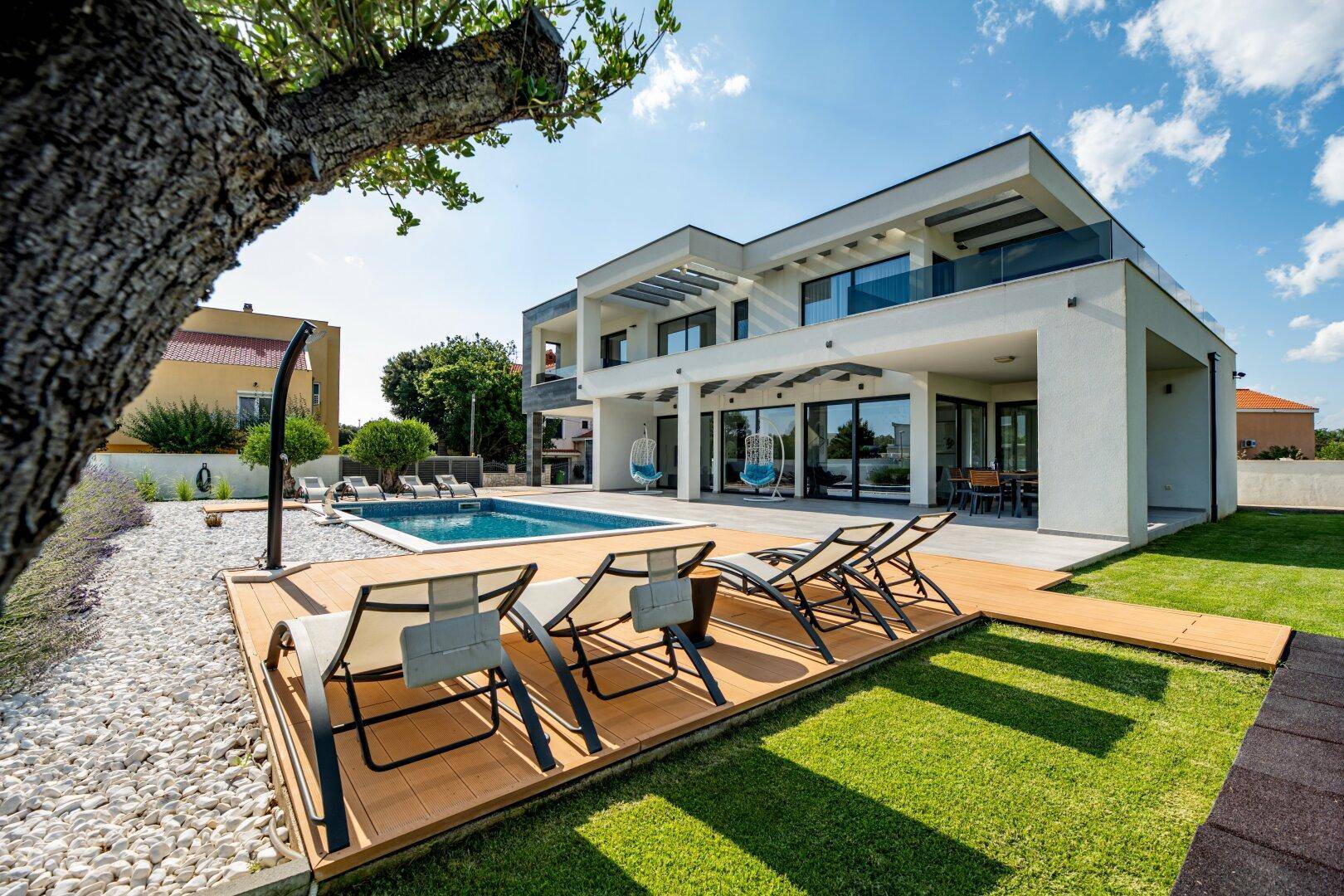 Gepflegter Gartenbereich mit Pool, Liegewiese und moderner Villa im Hintergrund.