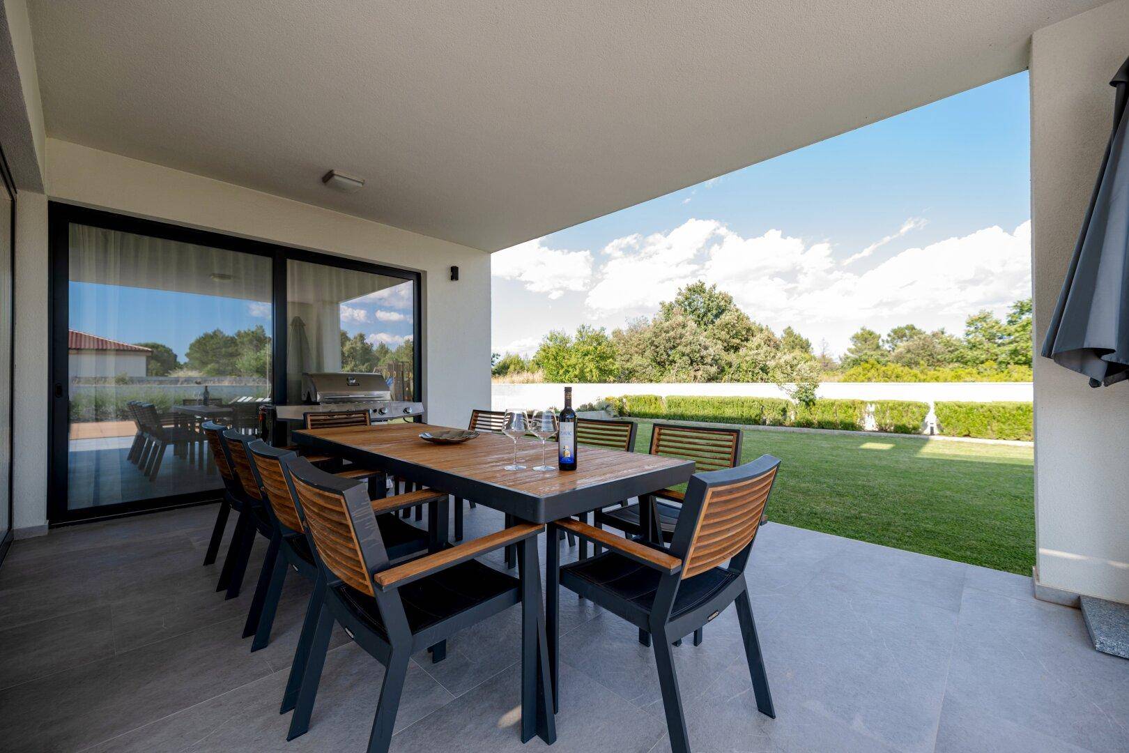 Überdachte Terrasse mit großem Esstisch, Grillbereich und Blick auf den Garten.