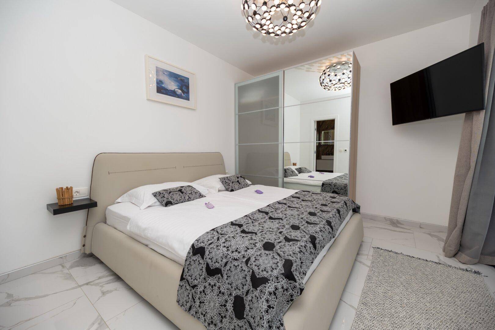 Helles Schlafzimmer mit Doppelbett, Spiegelschrank und modernem Deckenlicht.