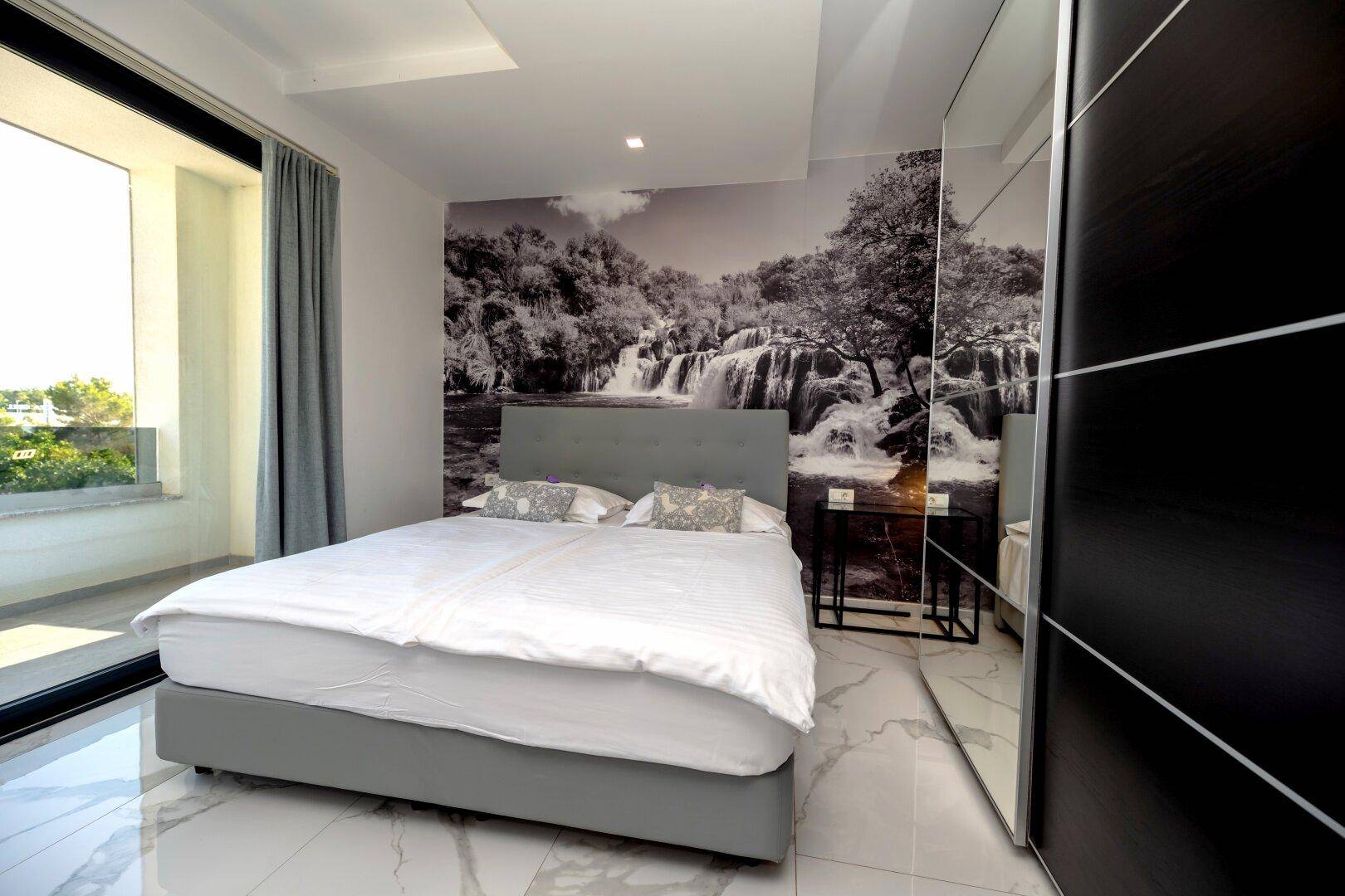 Schlafzimmer mit großem Bett, Schiebetüren zum Balkon und modernem Kleiderschrank.
