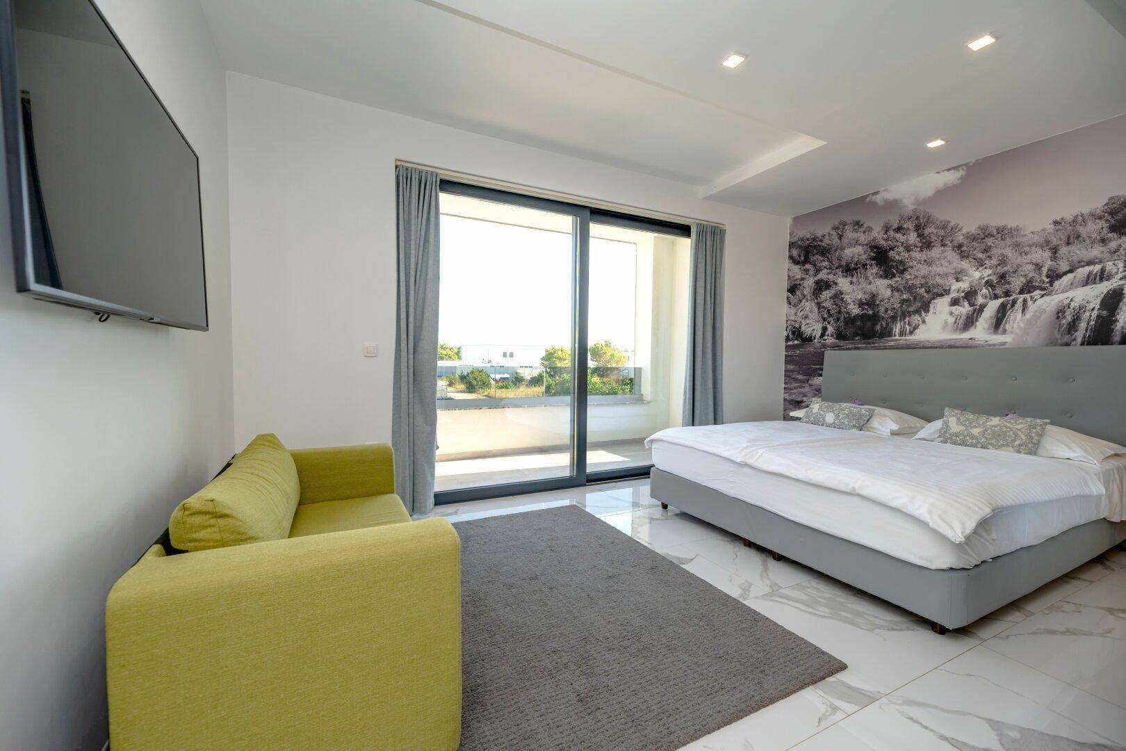 Helles Schlafzimmer mit Sofa, großem Bett und Schiebetüren zum Außenbereich.