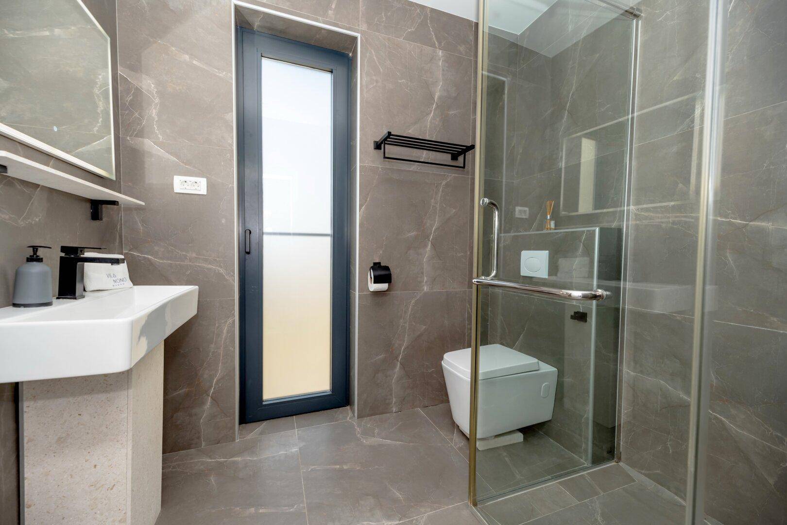 Modernes Badezimmer mit grauen Marmorfliesen, ebenerdiger Dusche und stilvollem Waschtisch.