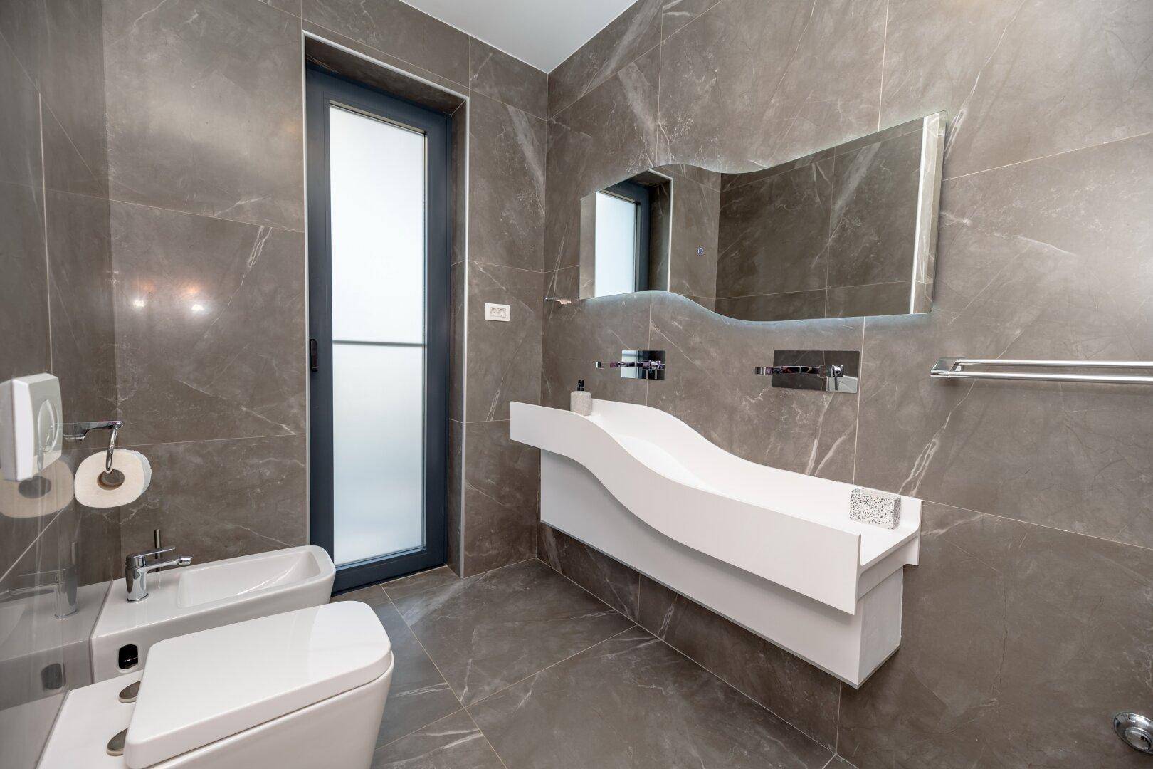 Elegantes Badezimmer mit modernem Waschtisch, beleuchtetem Spiegel und Bidet.