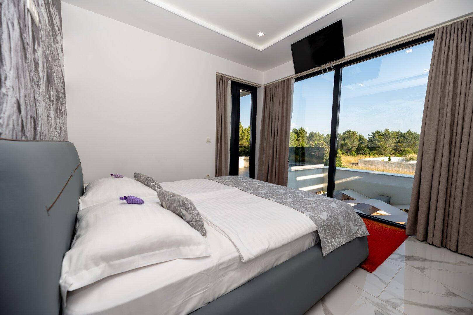 Schlafzimmer mit Doppelbett, großen Fenstern und Zugang zu einem privaten Balkon.