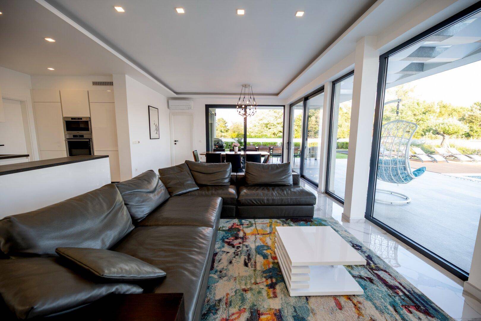 Geräumiger Wohn-Essbereich mit Ledersofa, farbigem Teppich und Zugang zur Poolterrasse.
