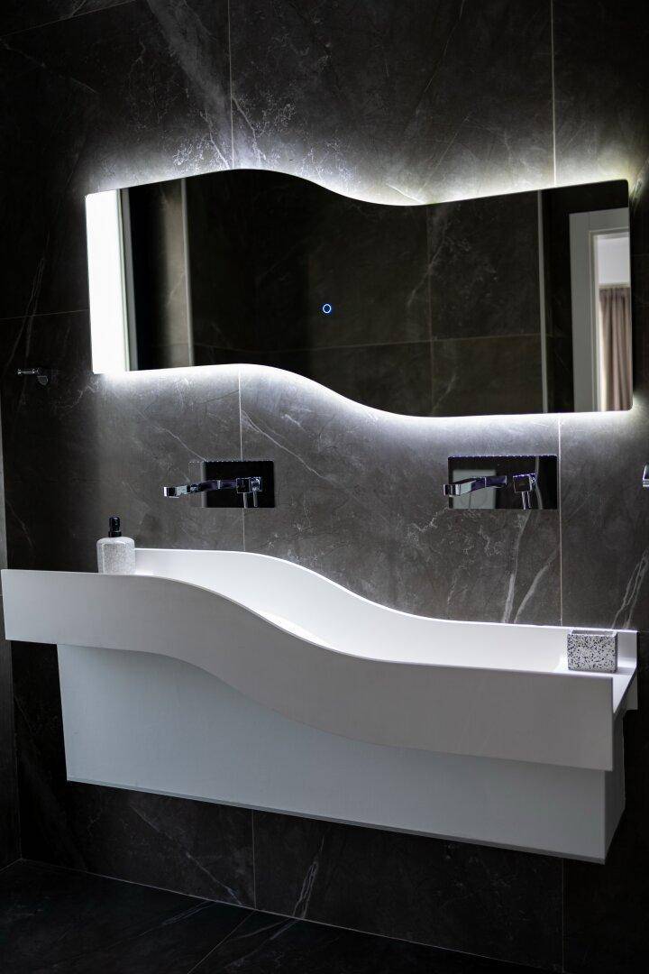 Elegantes Badezimmer mit modernem Waschtisch, beleuchtetem Spiegel und dunklen Fliesen.