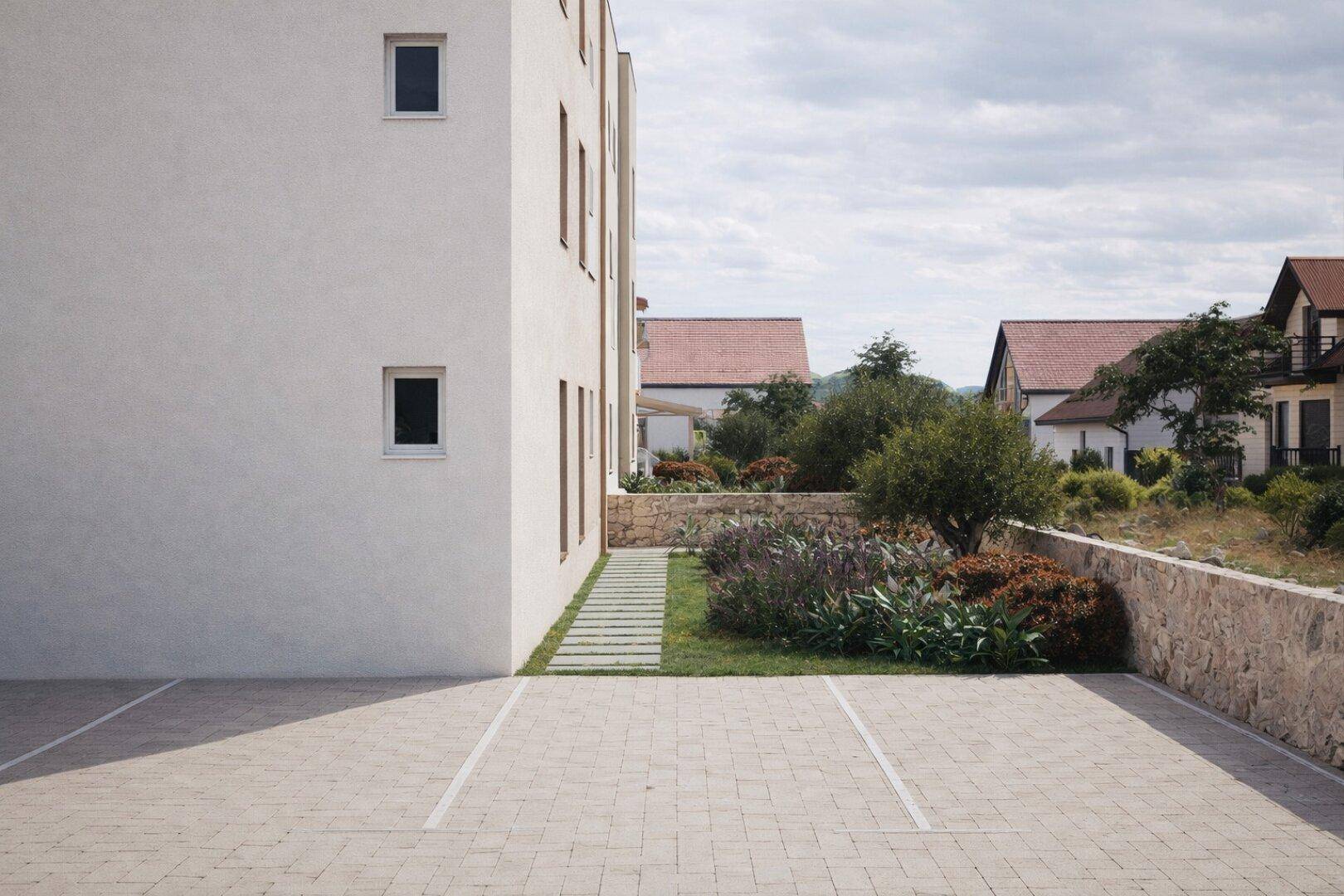 Gepflasterter Parkplatz neben dem modernen Gebäude mit angrenzender Grünfläche und Steinmauer.