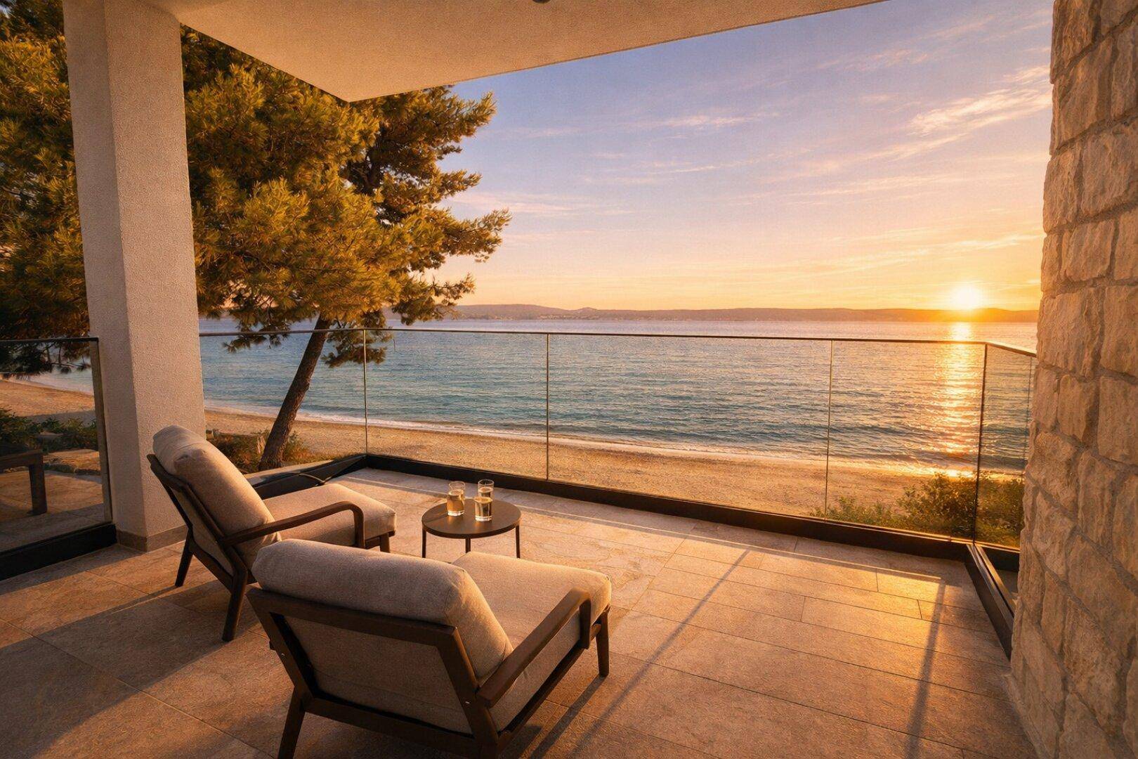 Möblierter Balkon mit Glasgeländer und atemberaubendem Meerblick bei Sonnenuntergang.