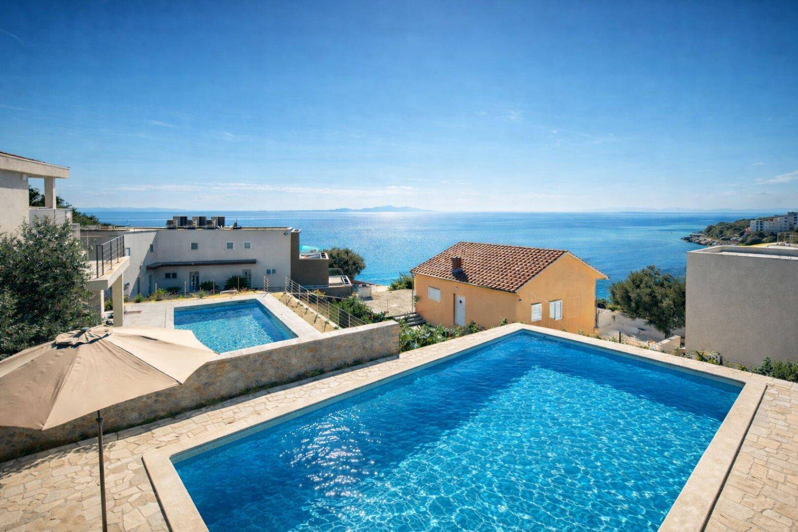Weitläufige Außenanlage mit mehreren Pools und atemberaubendem Meerblick unter blauem Himmel.