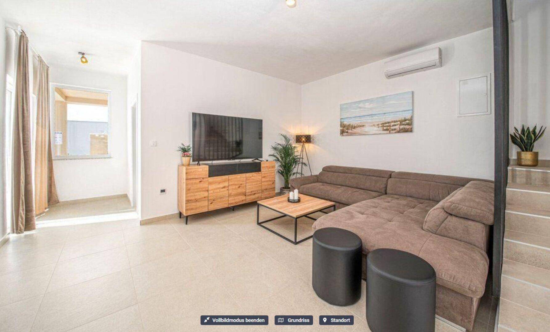 Gemütliches Wohnzimmer mit Ecksofa, modernem TV-Möbel und hellem Fliesenboden.