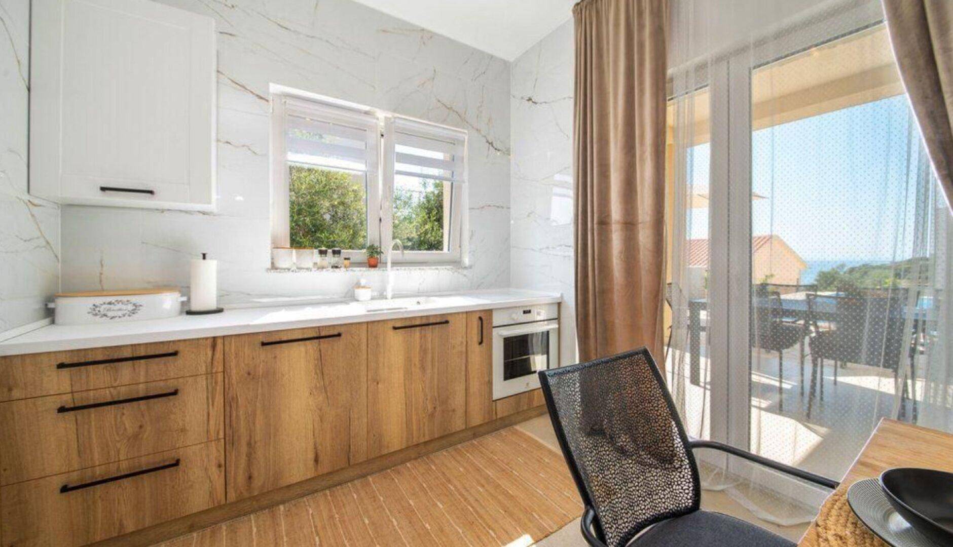 Moderne Küche mit Holzelementen, weißen Oberschränken und Zugang zur Terrasse mit Meerblick.