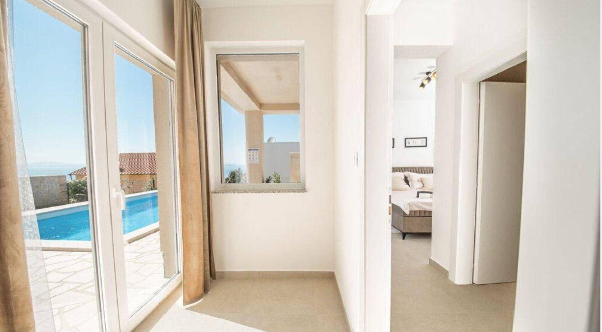 Heller Flur mit Zugang zum Schlafzimmer und großen Fenstern mit Blick auf den Poolbereich.
