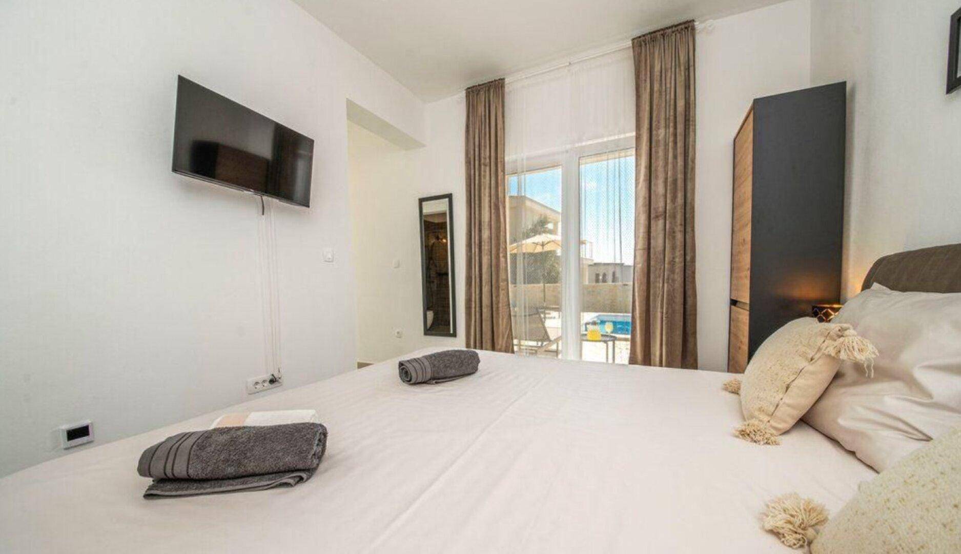 Gemütliches Schlafzimmer mit Doppelbett, TV und direktem Zugang zum Poolbereich.