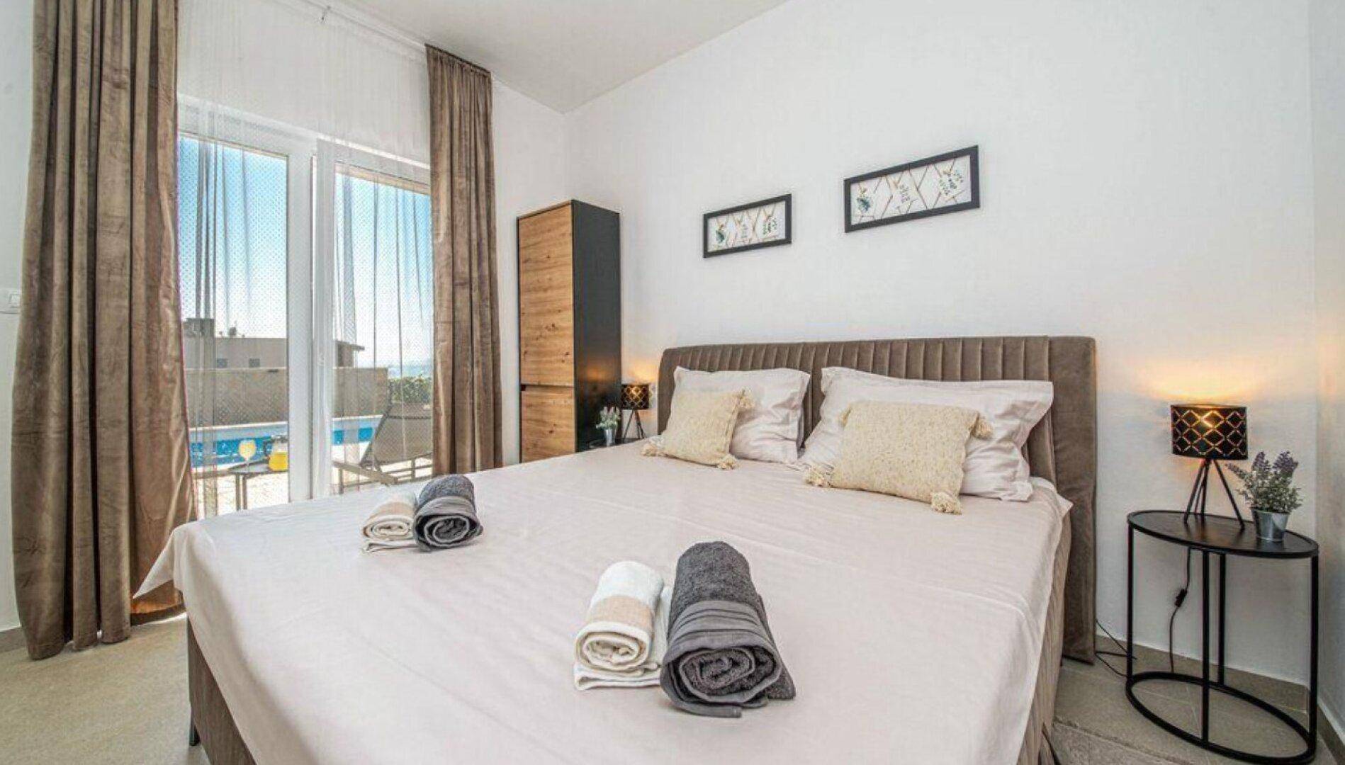 Helles Schlafzimmer mit großem Doppelbett, Nachttischen und Blick auf den Außenbereich.