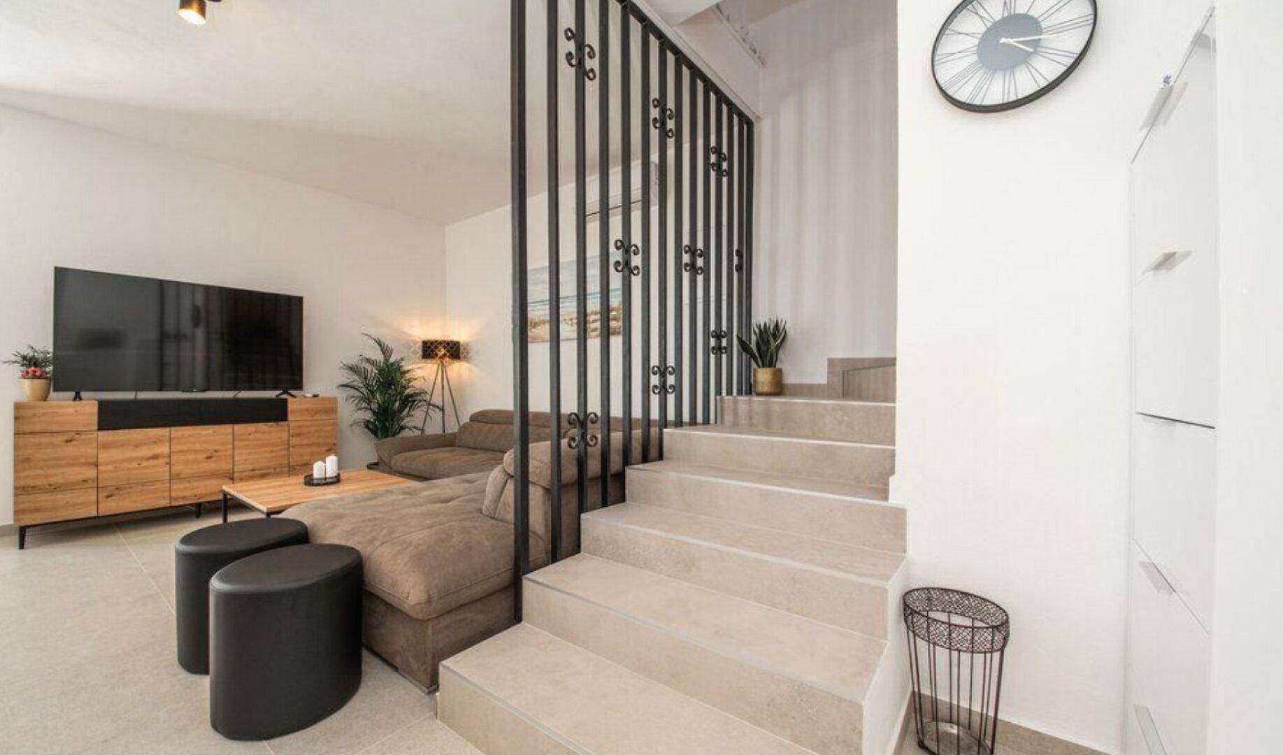 Wohnzimmer mit beigem Sofa, modernem TV-Möbel und Treppe mit schmiedeeisernem Geländer.
