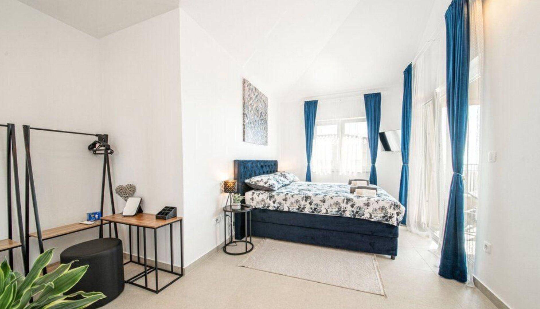 Modernes Schlafzimmer mit blauem Bett, floraler Bettwäsche und Balkonzugang.