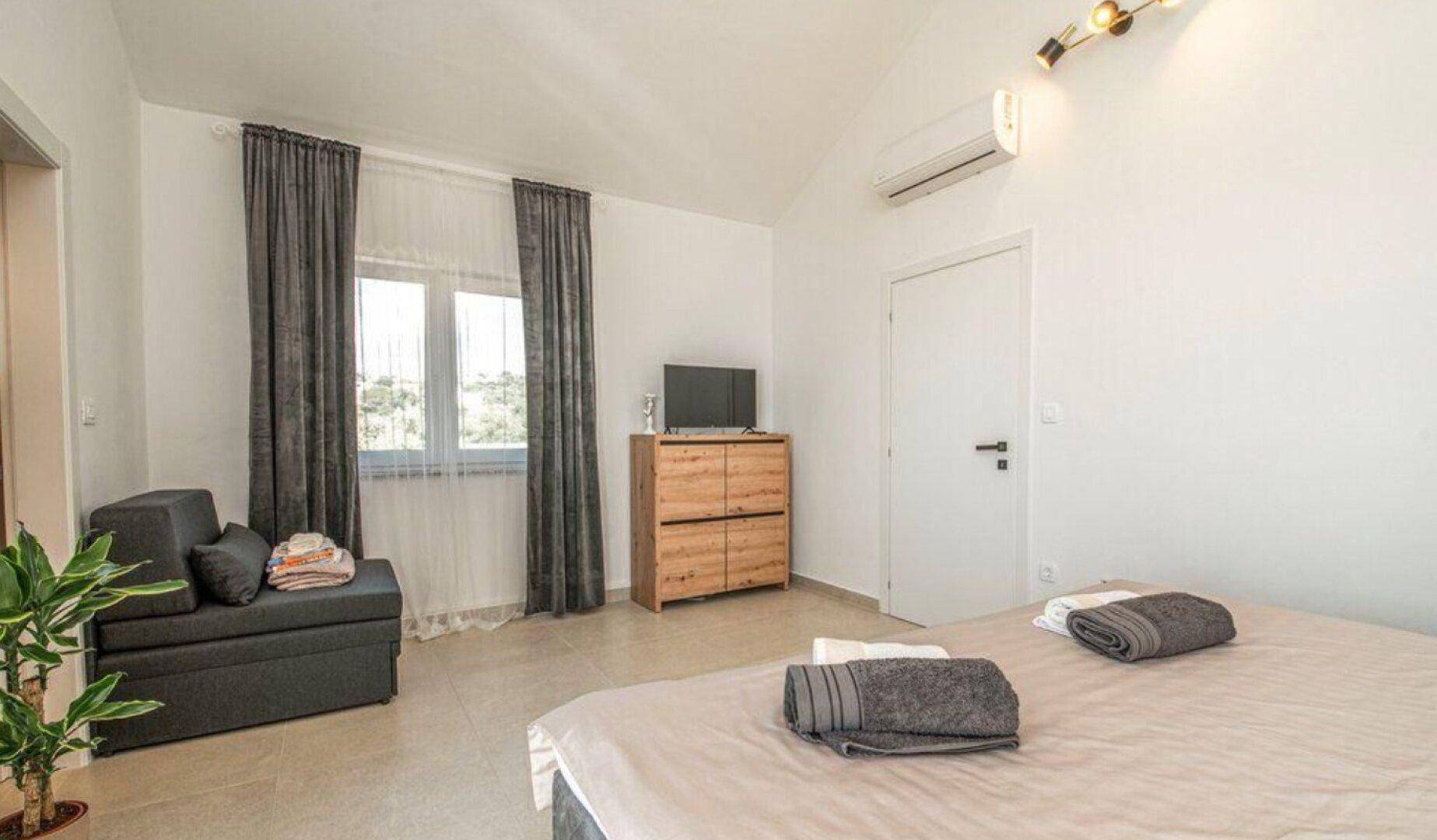 Helles Schlafzimmer mit Doppelbett, Sofa und Klimaanlage unter dem Dach.