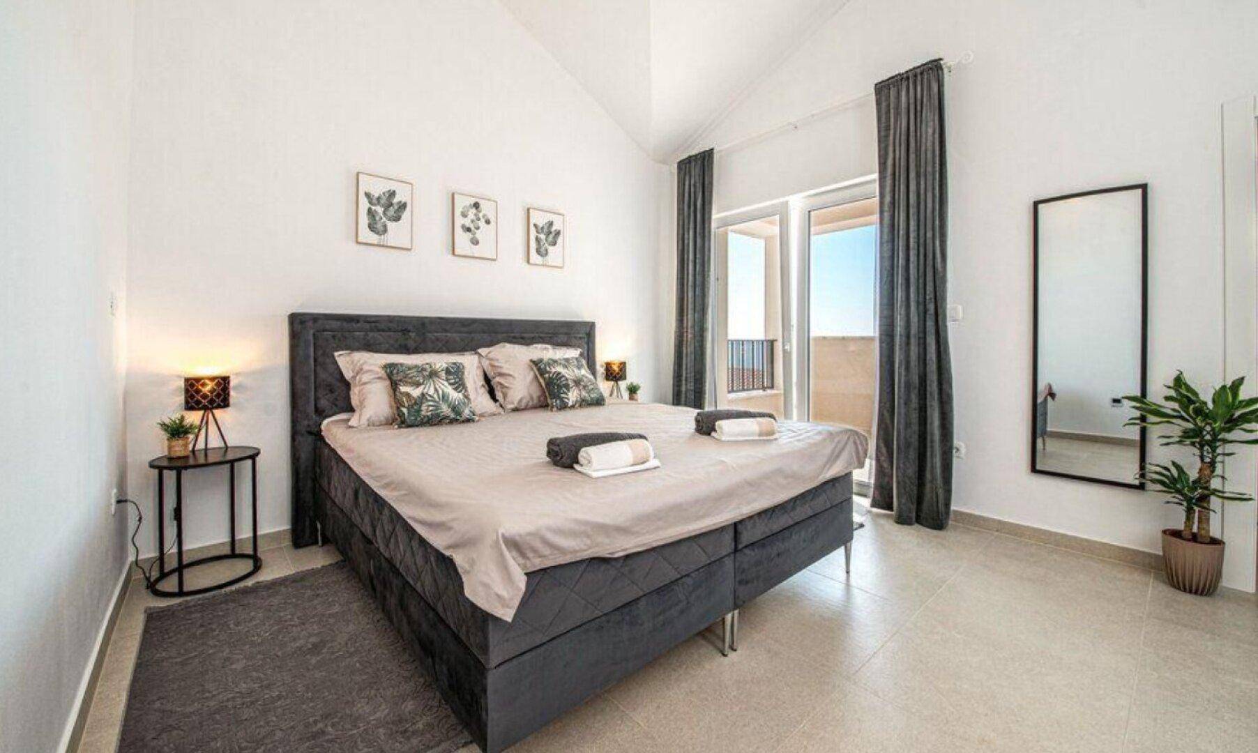 Geräumiges Schlafzimmer mit Doppelbett, Spiegel und Zugang zum Balkon.