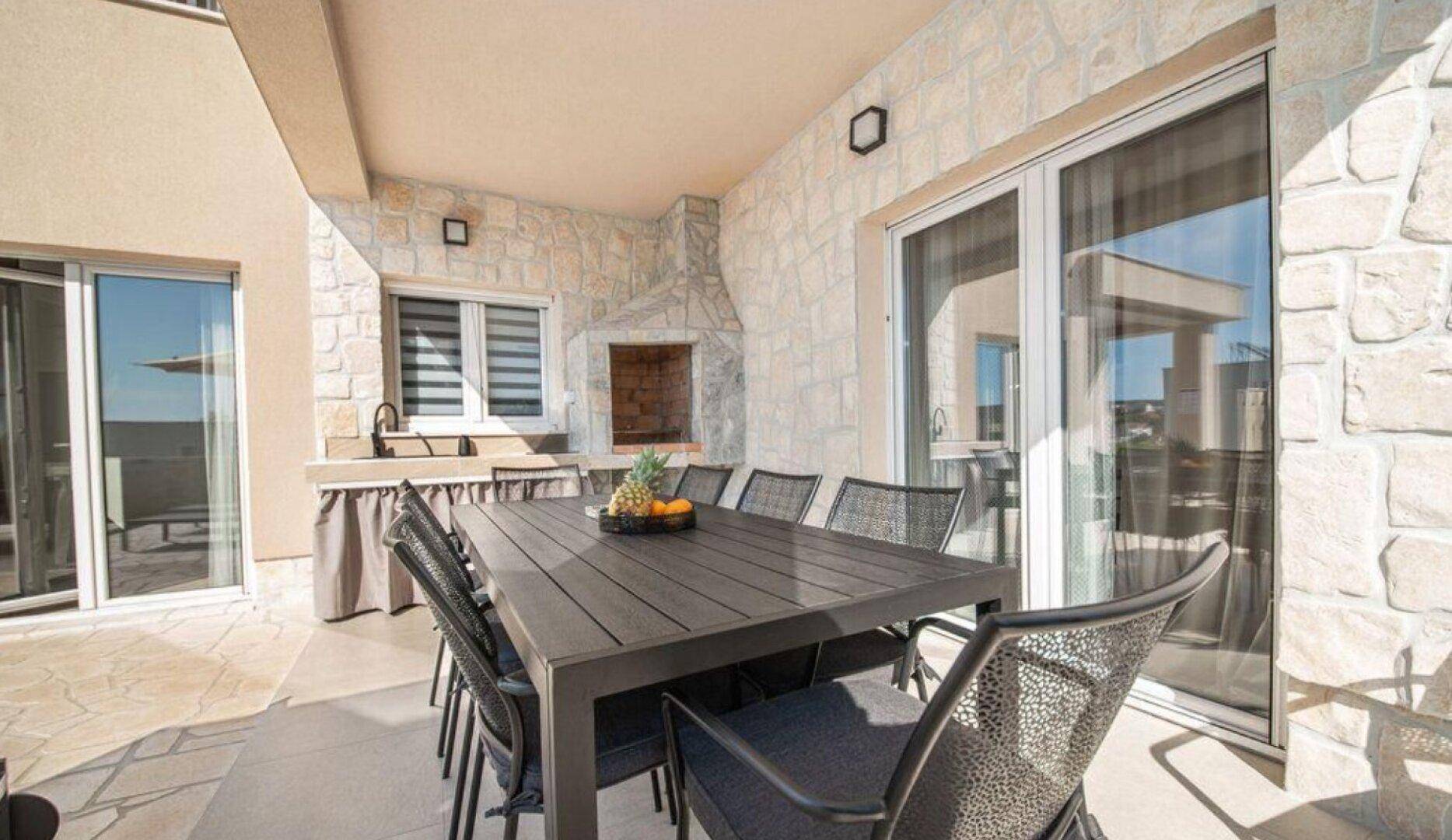 Überdachte Terrasse mit großem Esstisch, Außenküche und integriertem Grillbereich.