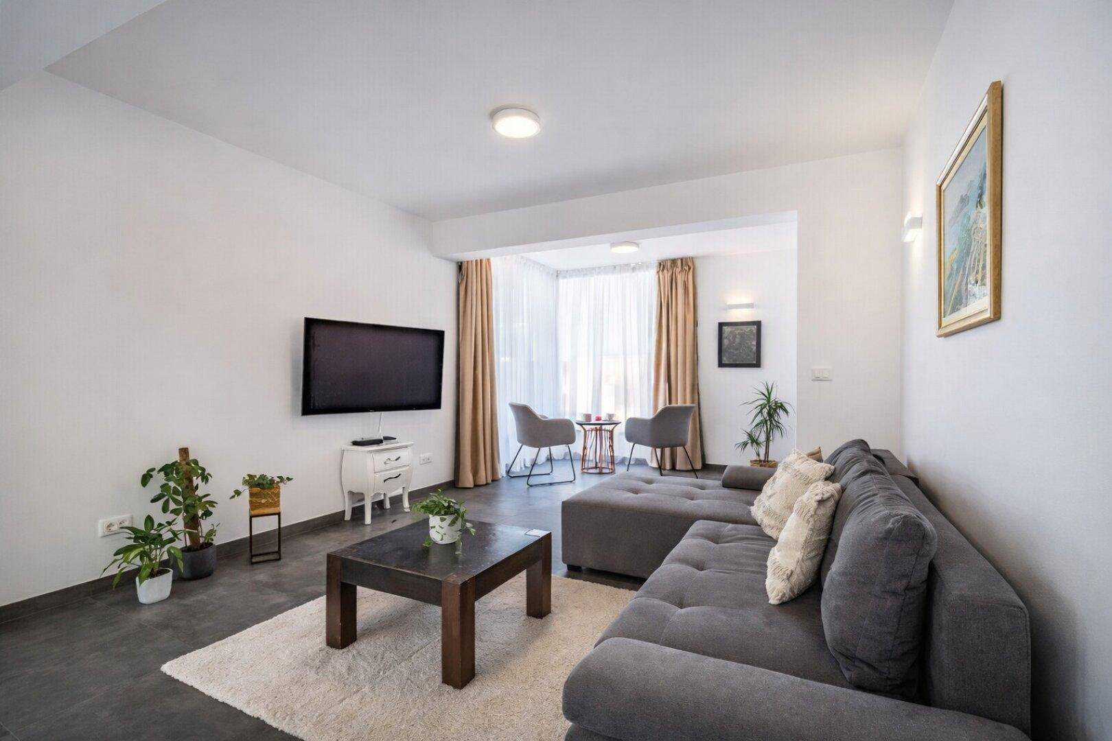 Modernes Wohnzimmer mit großem Sofa, Fernseher und Blick auf einen hellen Essbereich.
