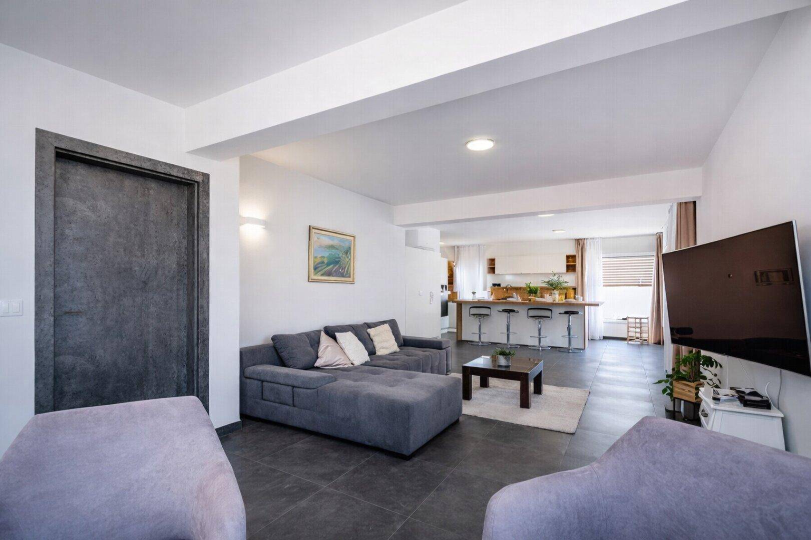 Offener Wohnbereich mit großem Sofa und Blick auf die moderne Küche mit Essbereich.