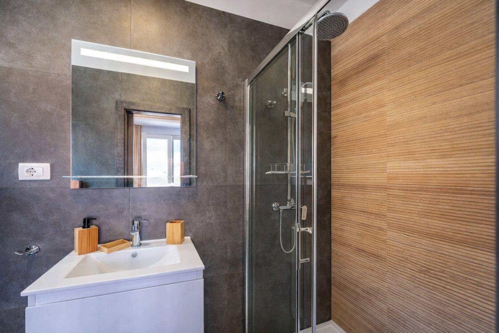 Modernes Badezimmer mit Duschkabine, Einzelwaschbecken und dunklen Fliesen an Wänden und Boden.