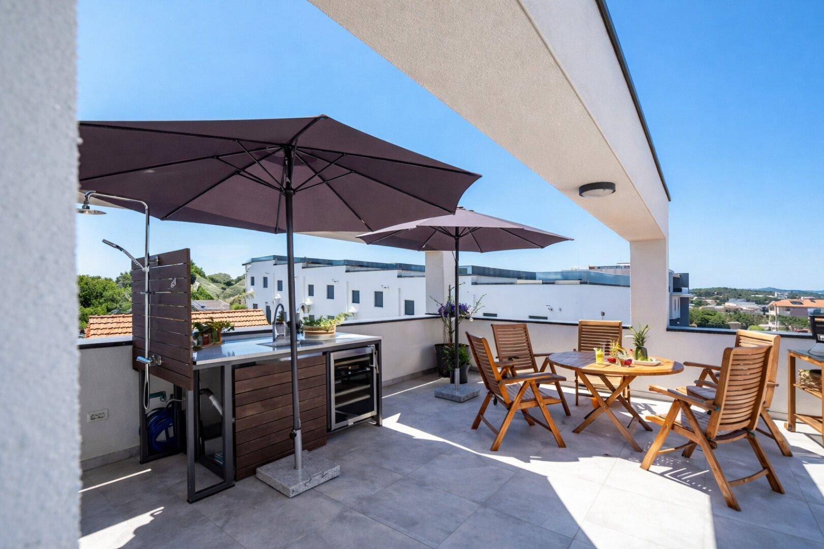 Sonniger Dachterrassenbereich mit Außenküche, Essbereich und weitem Blick über die Stadt.