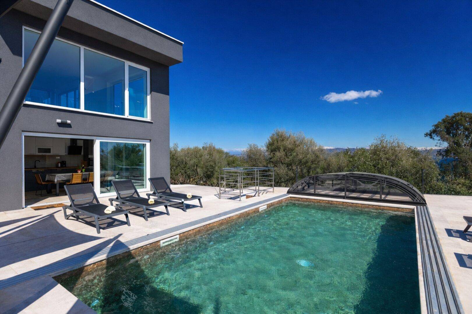 Außenansicht der modernen Villa mit Poolbereich und Liegestühlen unter blauem Himmel.