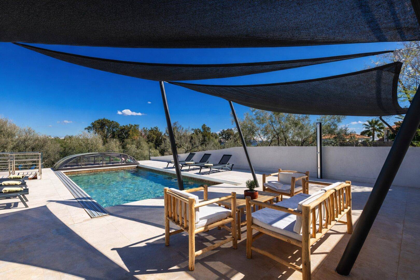 Gemütlicher Terrassenbereich mit Sitzgelegenheiten und Sonnensegel neben dem Pool.