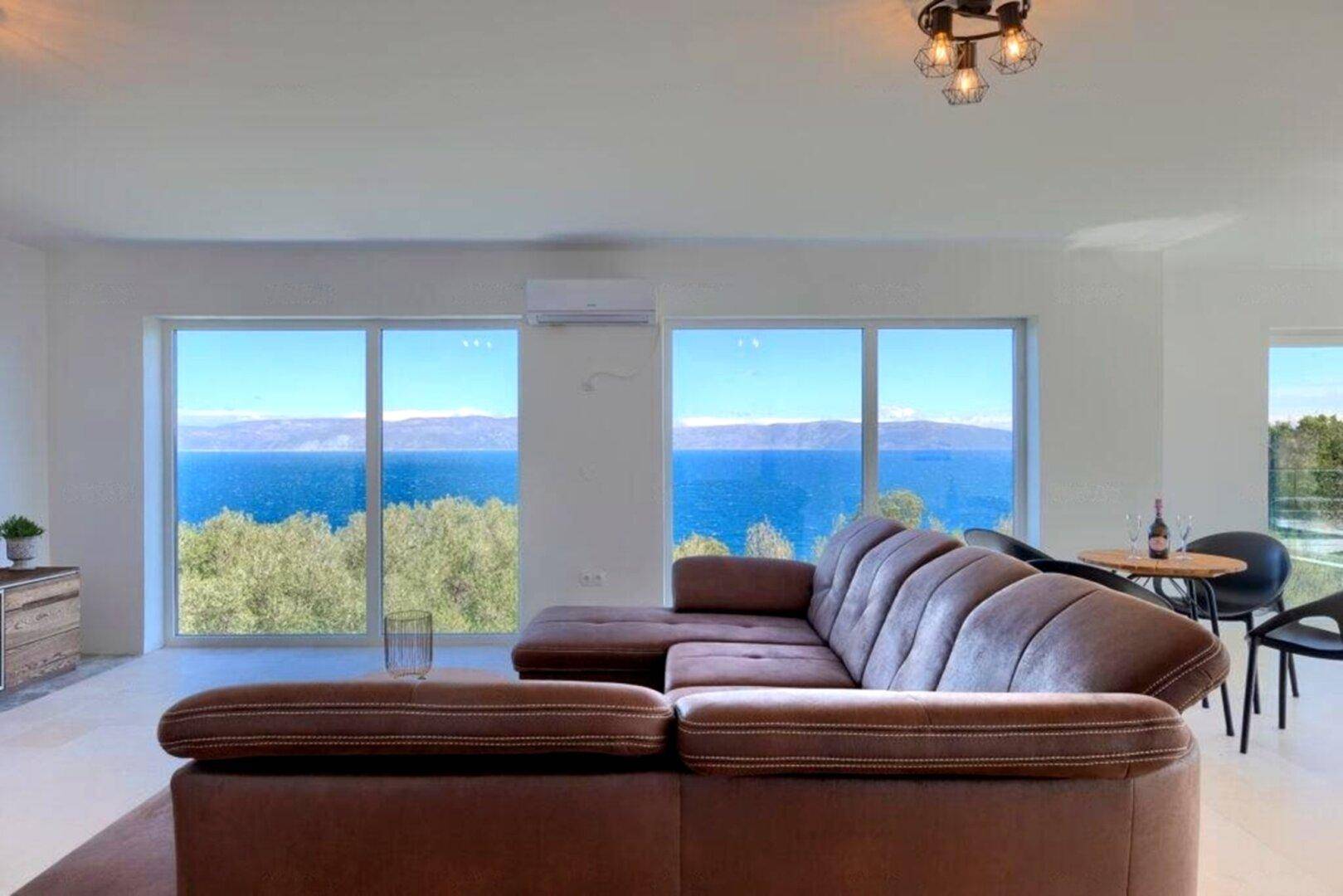 Helles Wohnzimmer mit bequemer Couch und Panorama-Meerblick durch große Fenster.
