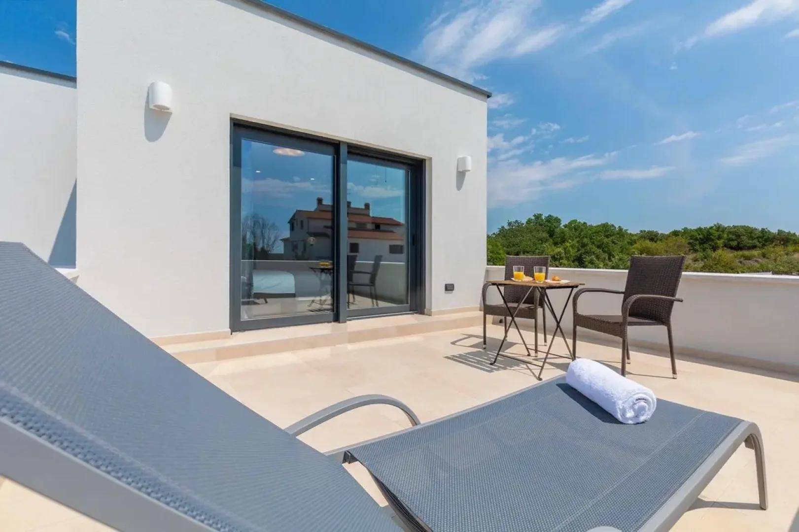 Weitläufige Dachterrasse mit Sonnenliegen und einer großen Glasschiebetür zum Innenbereich des Hauses.