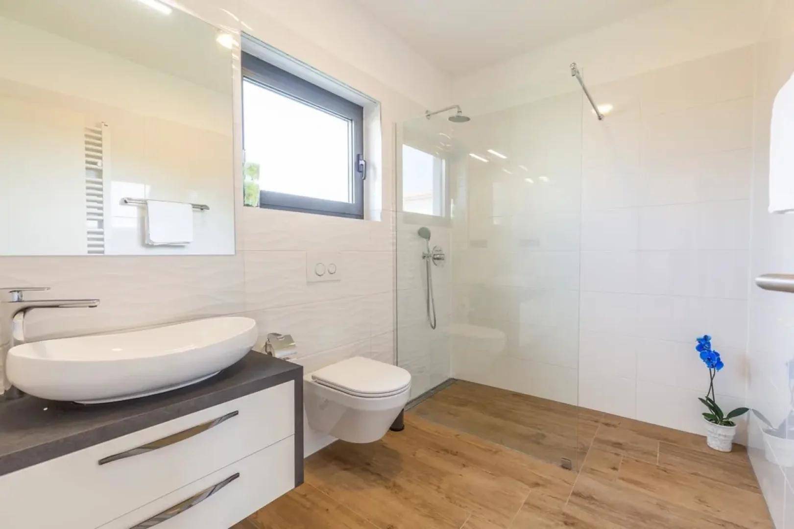 Modernes Badezimmer mit begehbarer Dusche, Aufsatzwaschbecken, wandhängendem WC und Fenster.