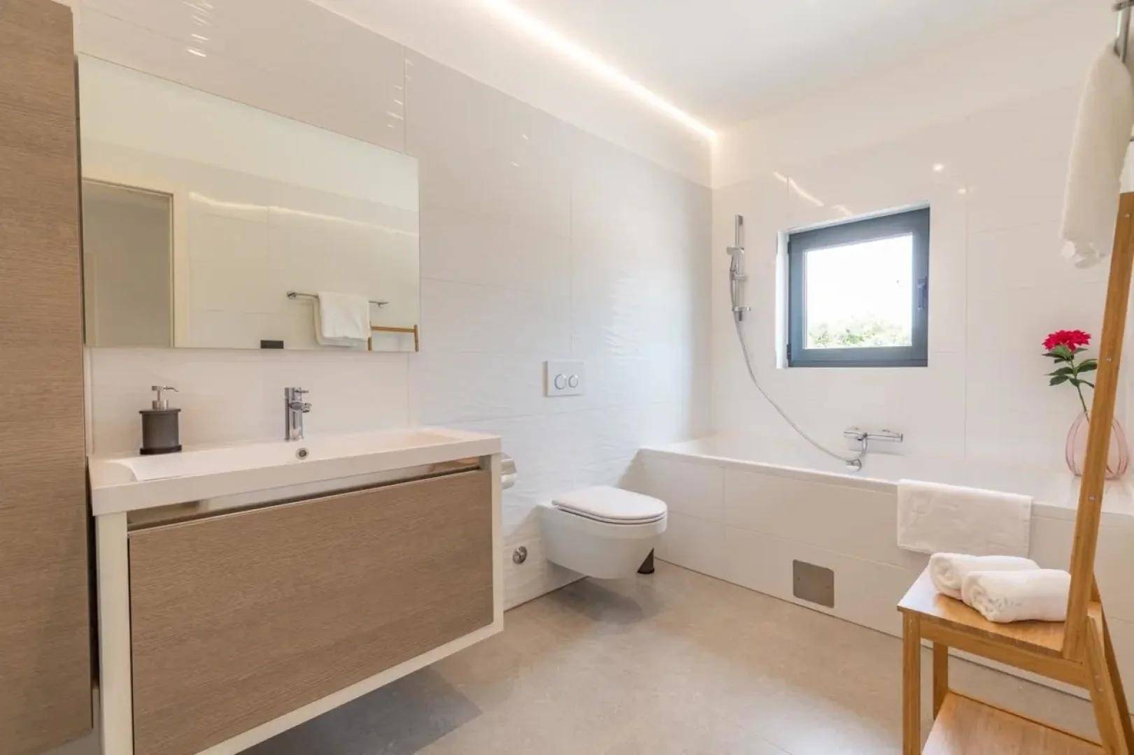 Modernes Badezimmer mit Badewanne, Waschtisch, wandhängendem WC und einem Fenster für Tageslicht.