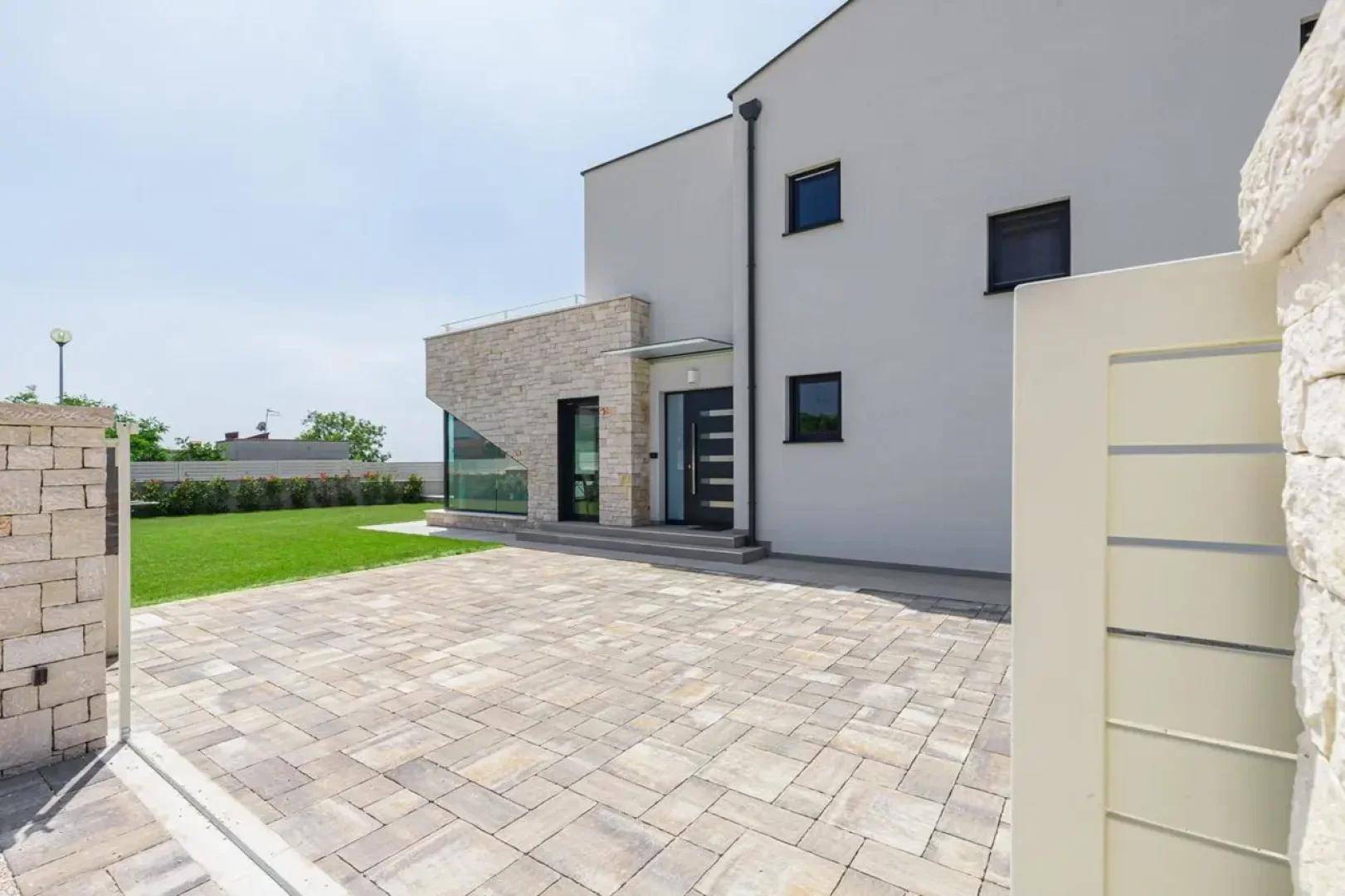 Vorderansicht des modernen Hauses mit gepflasterter Auffahrt und einem Eingangstor an einem sonnigen Tag.