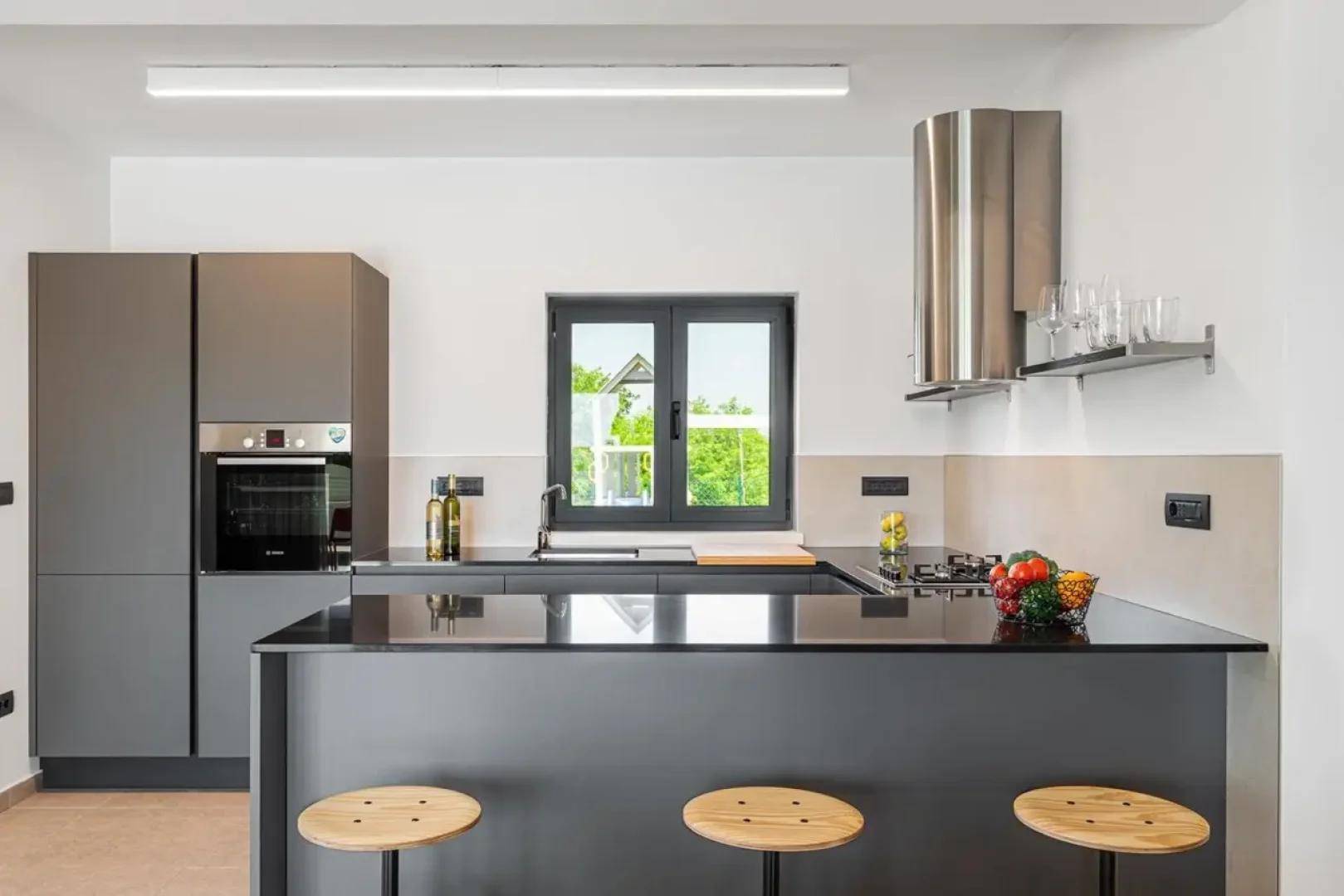 Moderne Küche mit grauen Schränken, schwarzer Arbeitsplatte und einem Fenster mit Blick ins Grüne.