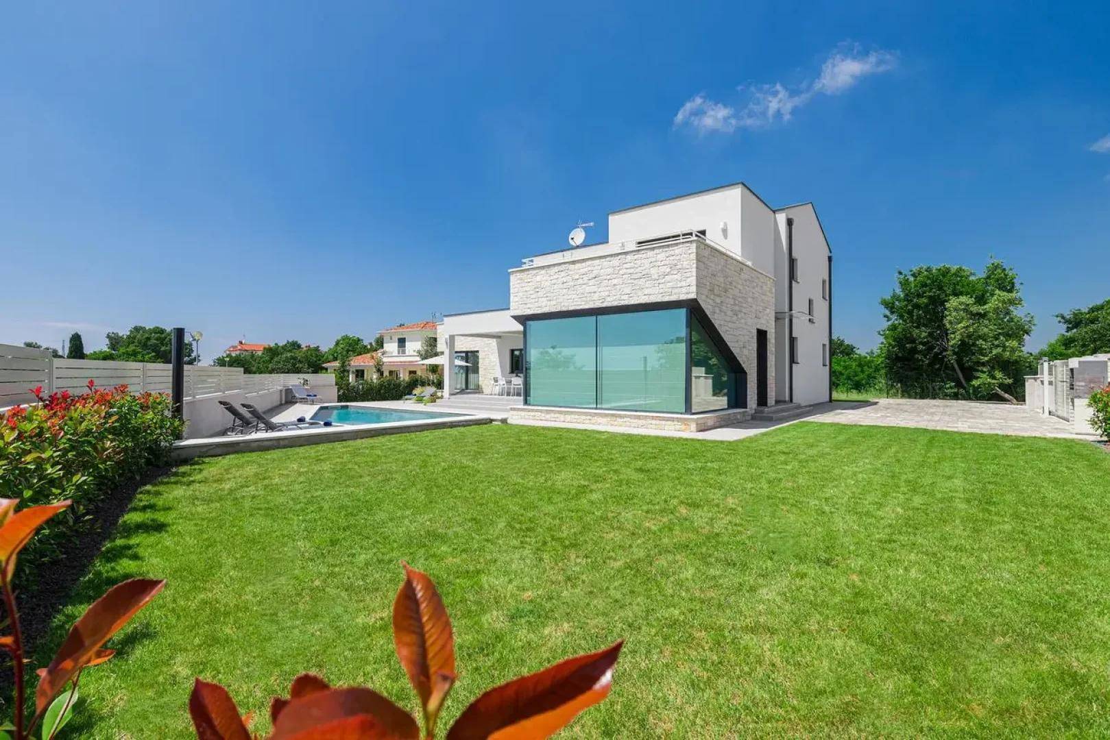 Modernes Haus mit großem Garten, Rasenfläche und privatem Swimmingpool unter blauem Himmel.