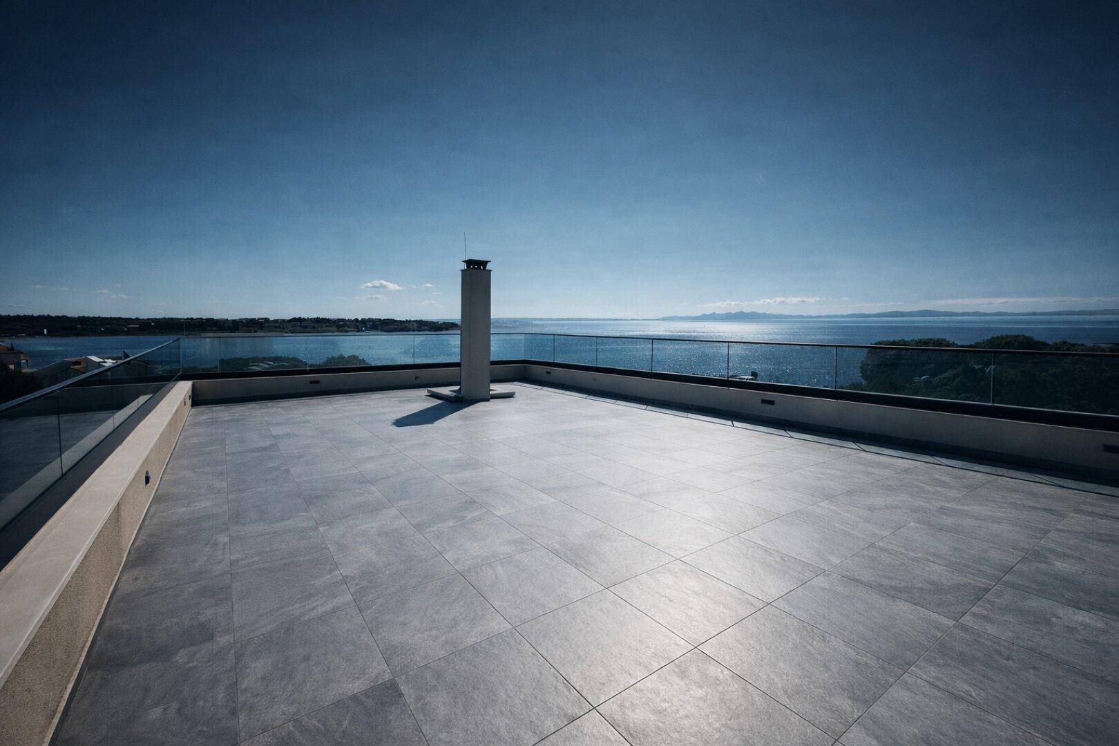 Große Dachterrasse mit Fliesenboden, Schornstein und Panoramablick auf das Meer.