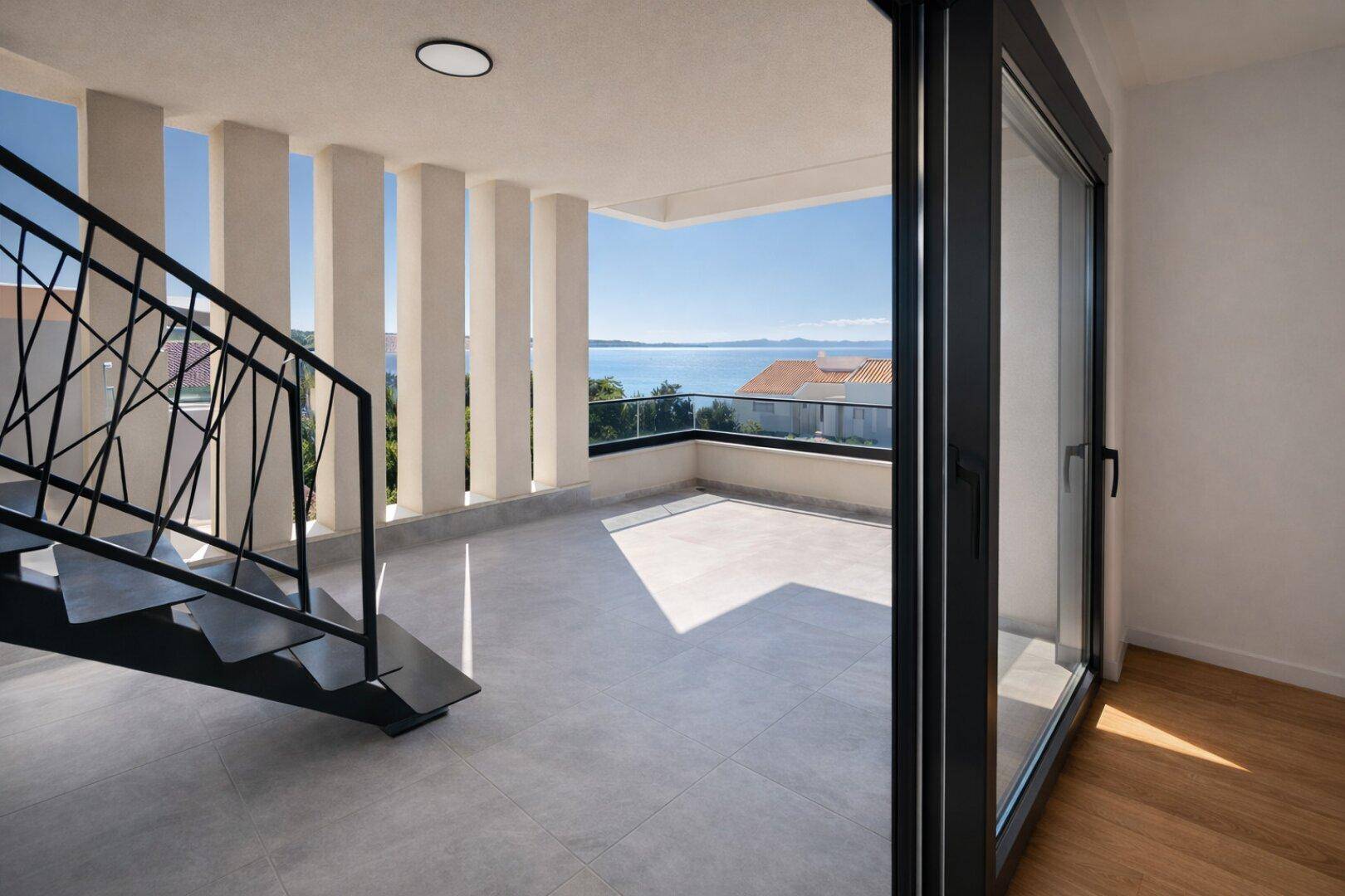 Geräumige Terrasse mit Meerblick, Säulen und Zugang zu Innenräumen über eine Schiebetür.