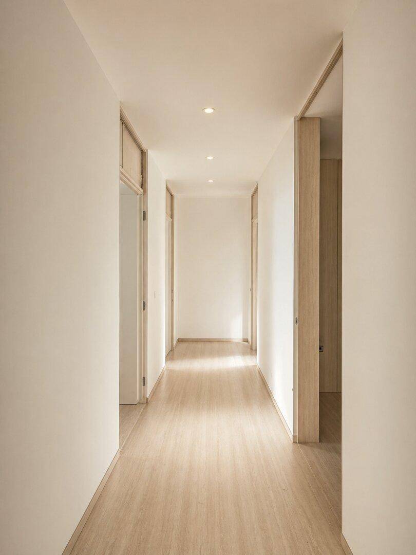 Langer, heller Flur mit Holzboden und indirekter Beleuchtung, der zu weiteren Räumen führt.