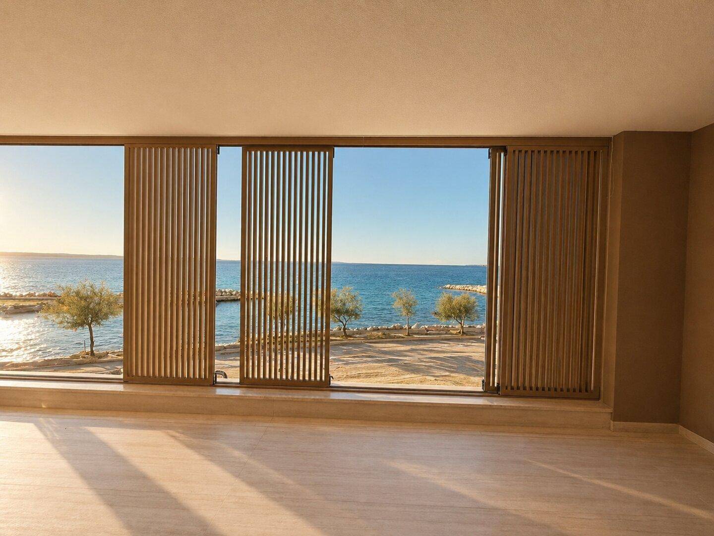 Heller Wohnraum mit großen Fenstern und Jalousien, die einen weiten Blick auf das Meer bieten.