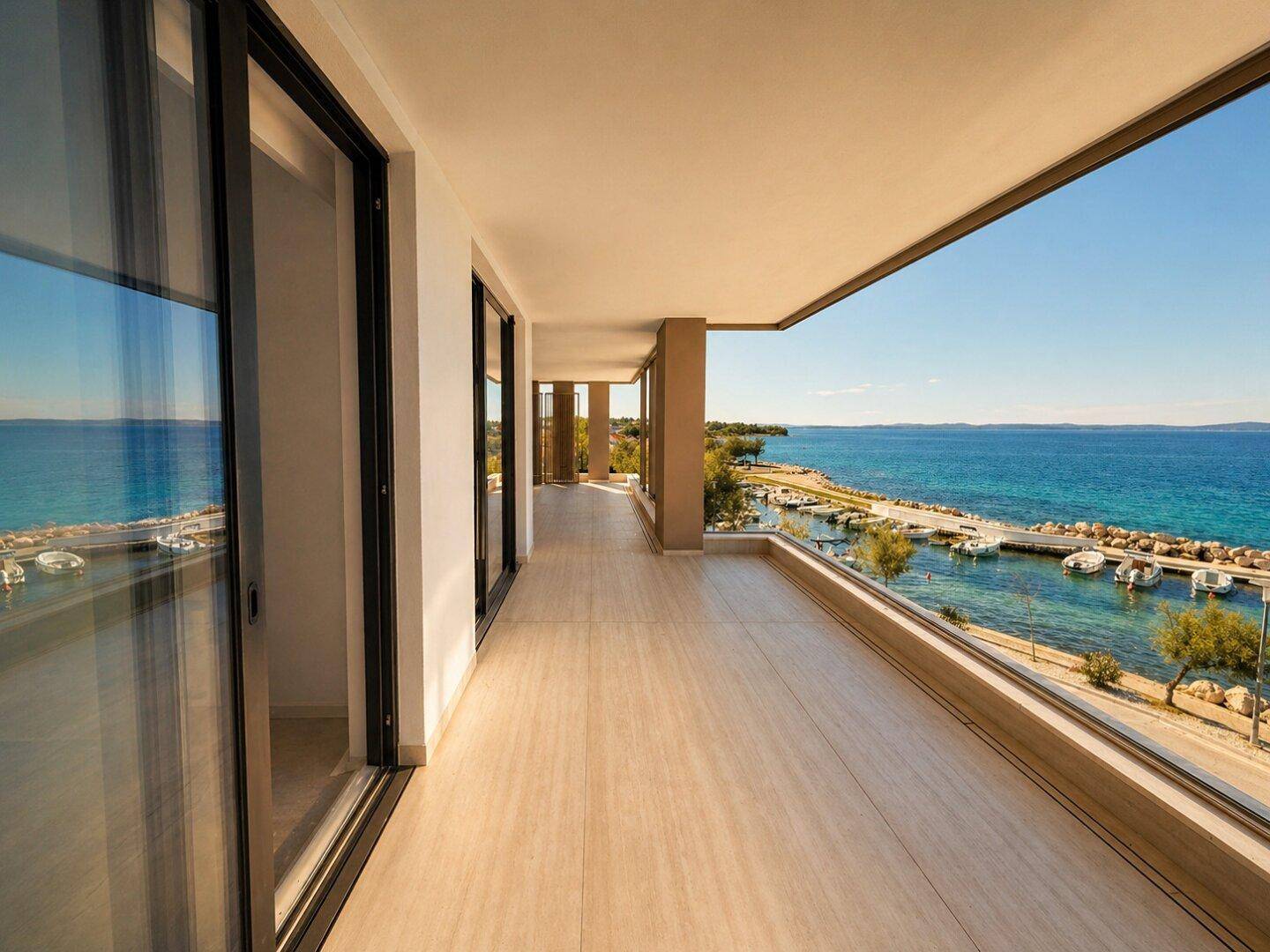 Langer Balkon mit Glasgeländer und weitem Blick auf das Meer und den Hafen.